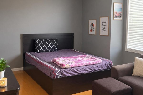 A bedroom with a dark wood bed frame, purple bedding, and framed art on a grey wall. - 6 Quincy Place N, Brampton