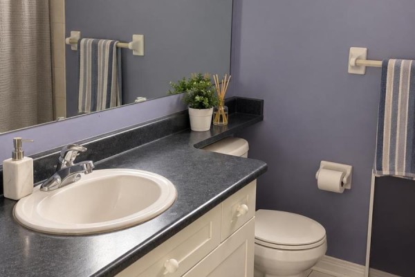 A bathroom vanity with a white sink, dark countertop, white cabinets, and toilet. - 6 Quincy Place N, Brampton