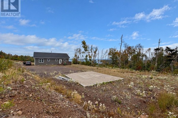 View of a house and driveway from a slight elevation, with a concrete pad and distant water. - 6 South West Crescent, Burin