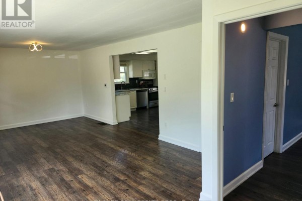 Open concept living area with dark wood floors, white walls, and a kitchen doorway. - 6 Sullivan Drive, New Tecumseth