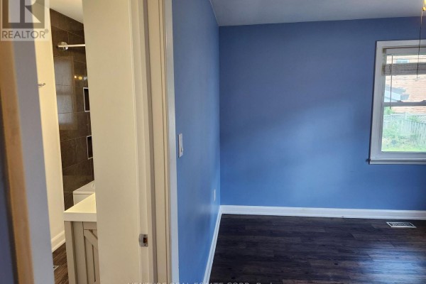 Bedroom with bright blue walls, dark wood floors, a window, and an open doorway to a bathroom. - 6 Sullivan Drive, New Tecumseth
