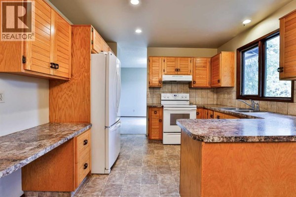 A spacious kitchen with light oak cabinets, a white refrigerator, white stove, and granite-look laminate countertops. - 6 Temple Boulevard W, Lethbridge