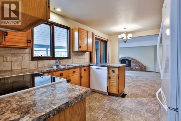 Kitchen view showing wood cabinets, beige tile flooring, stainless steel sink, and an adjacent living area with a fireplace. - 6 Temple Boulevard W, Lethbridge