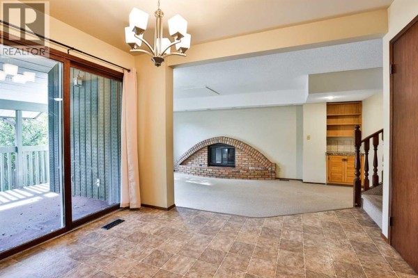 Dining area with sliding glass doors to a deck, view of a brick fireplace, built-in shelves, and staircase. - 6 Temple Boulevard W, Lethbridge