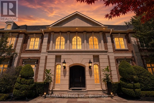 Front facade of a large brick and stone mansion with a grand entryway and symmetrical arched windows. - 6 The Bridle Path, Toronto