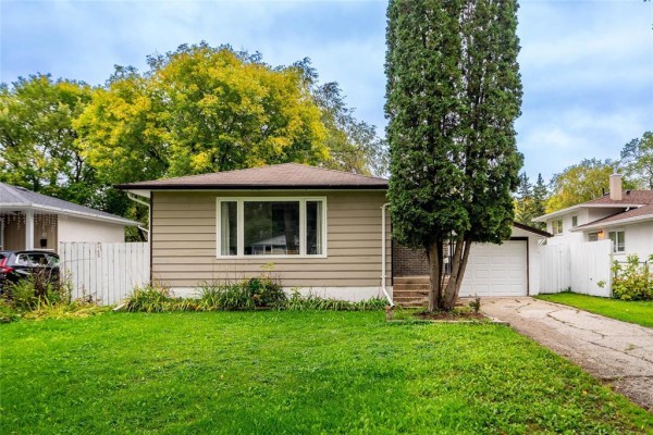 Side view of a beige bungalow with a white fence and mature trees. - 6 Tulane Bay, Winnipeg