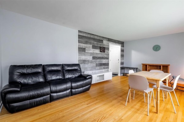 Living and dining area with a black leather sofa, light wood dining table, and wood plank accent wall. - 6 Tulane Bay, Winnipeg