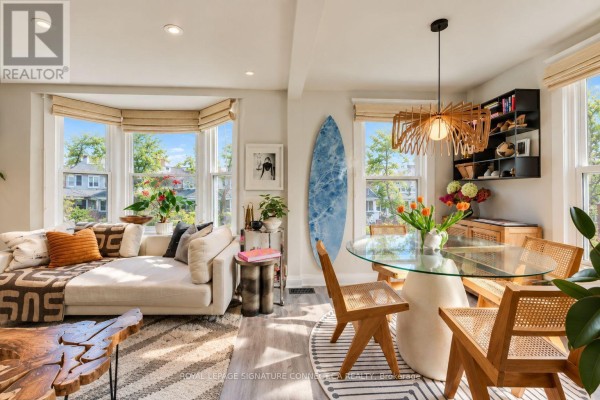 Living and dining area with bay windows, a white sectional sofa, glass dining table, and surfboard art. - 6 Wheeler Avenue, Toronto