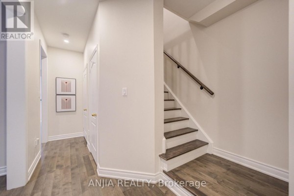 Hallway with wood-look flooring, two doors, and a staircase leading up. - 6 Wildmoor Street, Markham