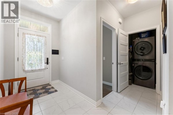 Interior entryway with a white door, stacked washer and dryer, and tile flooring. - 60 Andrew Lane, Thorold