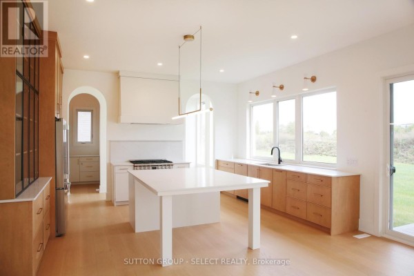 Modern kitchen with white island, wooden cabinets, and large windows for natural light. - 60 Bayshore Drive, Middlesex Centre