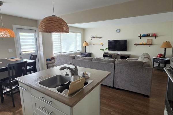 Living room with sectional sofa and television, adjacent to the kitchen area. - 60 Bradbrooke Drive, Yorkton