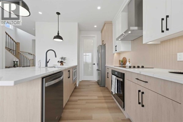 Spacious kitchen with an island, stainless steel appliances, light wood and white cabinetry, and staircase view. - 60 Bridges Drive Sw, Langdon