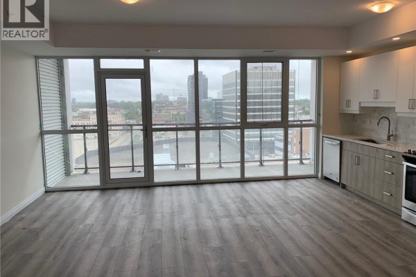Living room with grey flooring, a large window overlooking the city, and balcony door. - 60 Charles Street W Unit# 2409, Kitchener