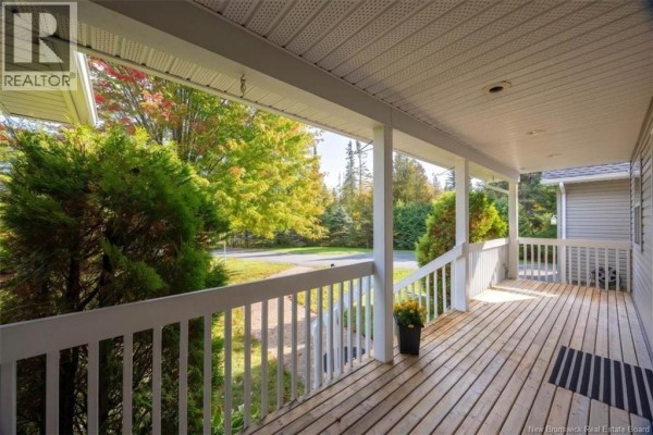 View from a covered wooden porch with white railings, looking towards the street and surrounding trees. - 60 Eldersley Avenue, Saint John