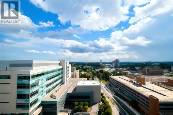 View from a high-rise apartment overlooking modern buildings and a distant cityscape under a cloudy sky. - 60 Frederick Street Unit# 1401, Kitchener