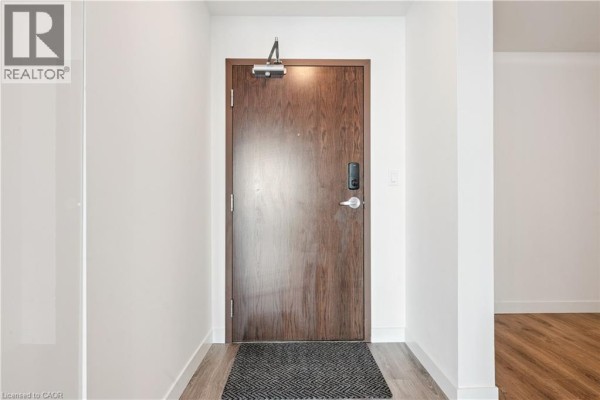 Dark wood apartment entrance door with a digital lock and a grey doormat on a wood-look floor. - 60 Frederick Street Unit# 2913, Kitchener