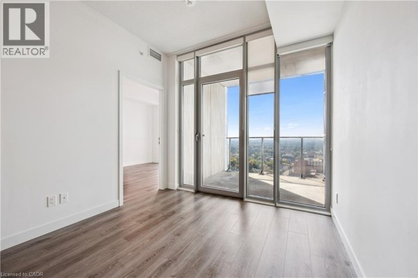 Bedroom with a large glass sliding door leading to a balcony, overlooking a cityscape with trees. - 60 Frederick Street Unit# 2913, Kitchener