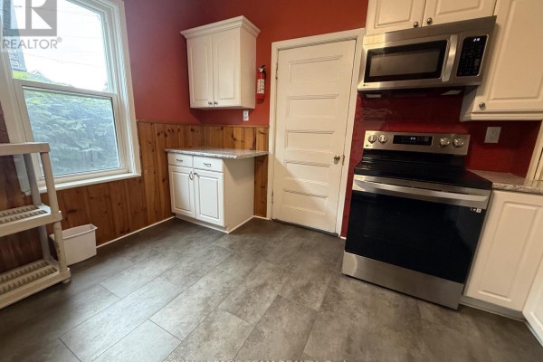 Kitchen with white cabinets, stainless steel stove, dishwasher, and wood paneling on the wall. - 60 Herridge Street, Ottawa