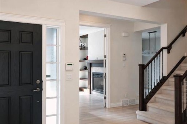 Foyer with a black front door, view into a hallway with stairs and a gas fireplace. - 60 Hong Kong Road Sw, Calgary
