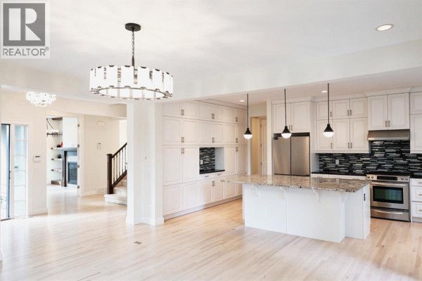 Open concept living space with a kitchen island, white cabinets, and light hardwood floors. - 60 Hong Kong Road Sw, Calgary