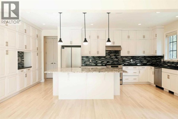 Spacious kitchen with white cabinetry, granite island, stainless steel appliances, and hardwood floors. - 60 Hong Kong Road Sw, Calgary
