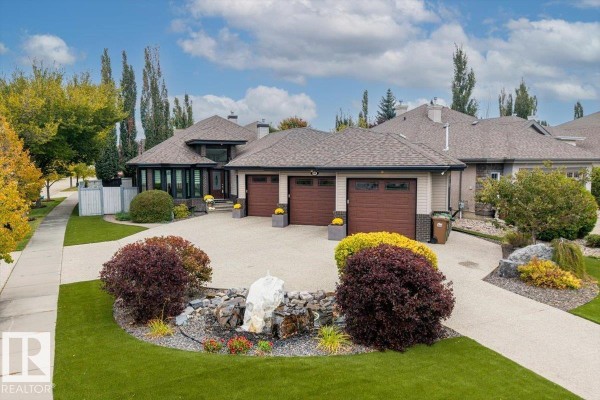 St. Albert home exterior with a triple garage, driveway, and manicured landscaping under a cloudy sky. - 60 Lafleur Dr, St  Albert