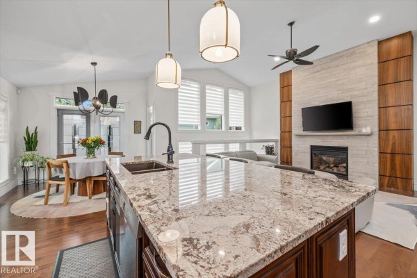 Kitchen island with granite countertop and pendant lights overlooking a living room with a stone fireplace and television. - 60 Lafleur Dr, St  Albert