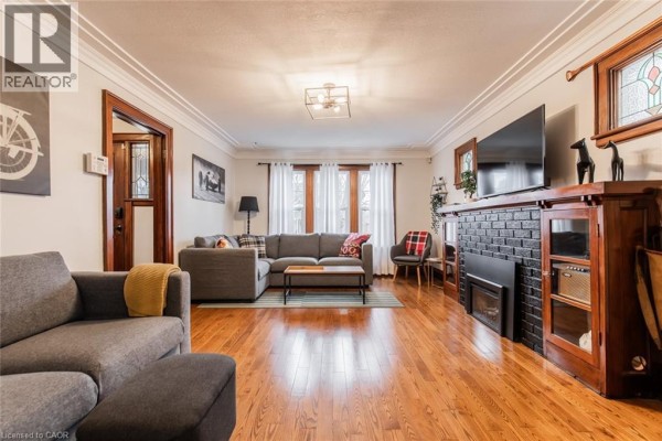 Living room with a grey sectional sofa, fireplace, hardwood floors, and large windows. - 60 Lake Avenue Drive, Stoney Creek