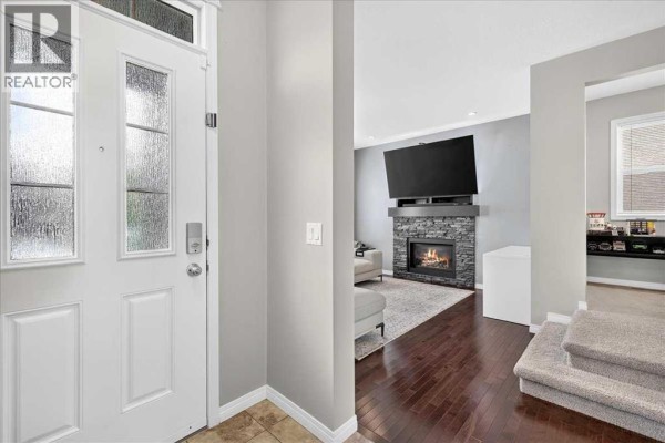 View from the front door into a living room with a stone fireplace, television, and wood floors. - 60 Mahogany Grove Se, Calgary