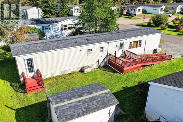 Aerial view showing the side and back of a beige mobile home with red decks, a gravel driveway, and surrounding homes. - 60 Midway, Moncton
