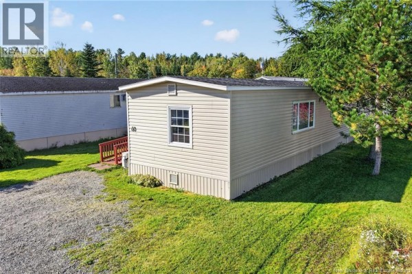 Side view of a beige mobile home with tan siding, white trim windows, and a red staircase, set on a green lawn. - 60 Midway, Moncton