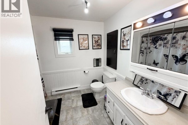 Bathroom with white vanity, white wainscoting, toilet, and a floral shower curtain. - 60 Normandie Street, Petit Rocher