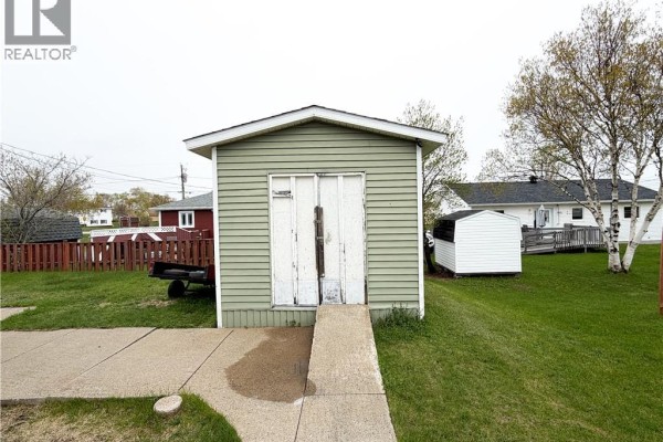 Small, light green shed with double white doors and a concrete ramp in the yard. - 60 Normandie Street, Petit Rocher