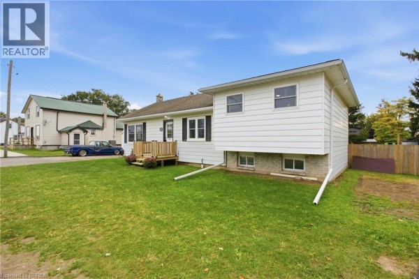 Side exterior view of the white bungalow, showing the foundation and lawn. - 60 Railway Street W, Princeton