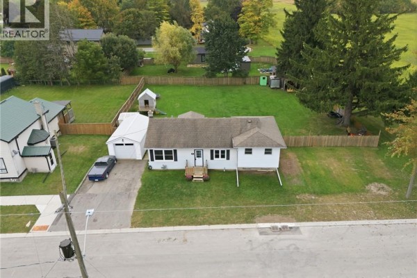 Aerial view of the white bungalow, detached garage, and surrounding grassy yard. - 60 Railway Street W, Princeton