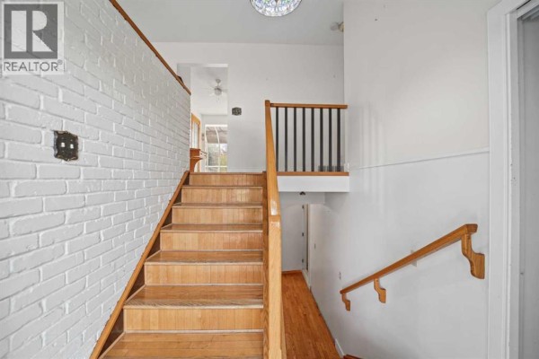 Interior staircase with wood treads and white brick accent wall. - 60 Silverview Way Nw, Calgary