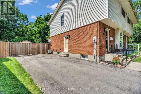 Side view of the house showing the driveway, wooden fence, and backyard access. - 60 Tilipe Road, London East