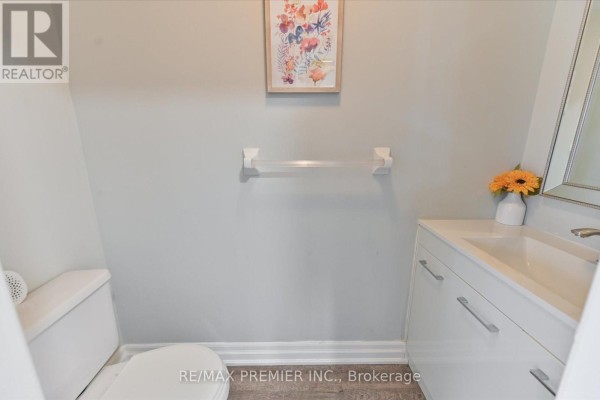 Powder room with a toilet, white vanity, sink, and a framed floral art print. - 60 Tumbleweed Court, Vaughan