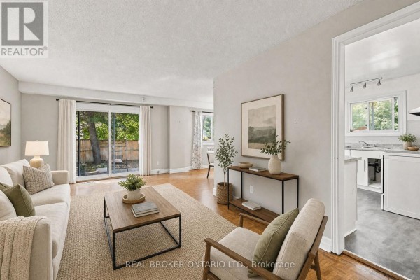 Living room with beige sofa and armchair, coffee table, rug, and doorway to kitchen. - 60 Tybalt Crescent, Ottawa