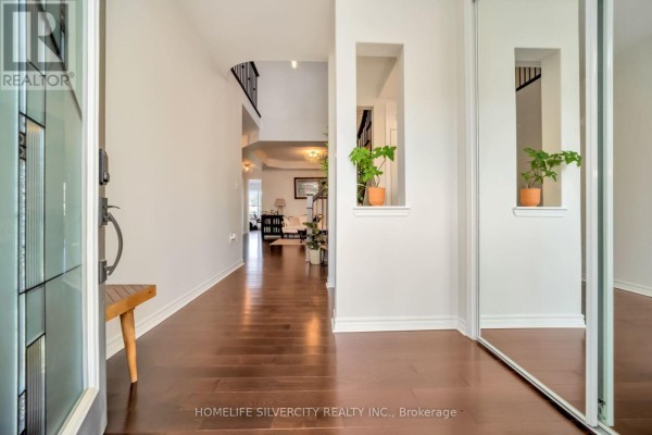 Interior view of a hallway with dark wood floors, white walls, and mirrored closet doors. - 60 Tysonville Circle, Brampton