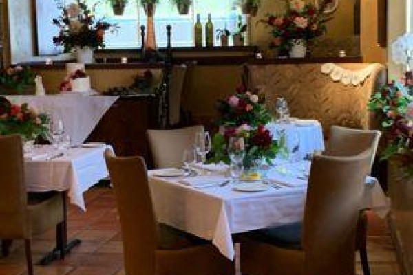 Restaurant tables set with white tablecloths, floral centerpieces, and chairs with brown upholstery. - 60 Walnut Street, Hamilton