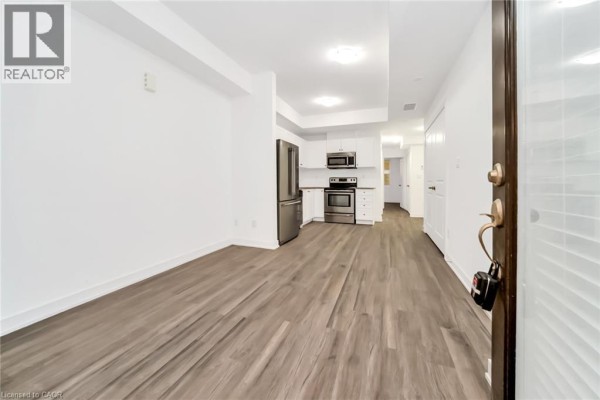Living room with wood-look flooring, white walls, and a small kitchen area. - 60 Winston Park Boulevard Unit# 60, Toronto