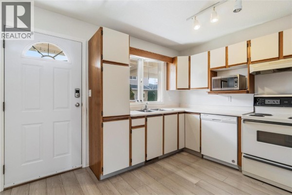 Kitchen with white cabinets, double sink, and a window overlooking the yard. - 600 10 Street Sw Unit# 6, Salmon Arm