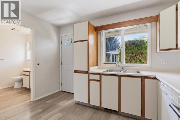 Kitchen with a window, white cabinets, and doorway to a bathroom with a toilet. - 600 10 Street Sw Unit# 6, Salmon Arm