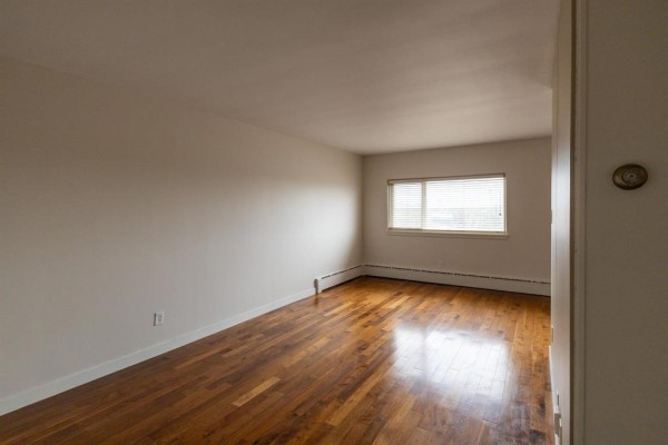 Interior of a room with white walls, a window with blinds, and dark wood flooring. - 600 565 Corydon Avenue, Winnipeg