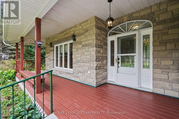 Covered front porch with red decking, stone walls, and double glass front doors. - 600 Crozier Road, North Grenville