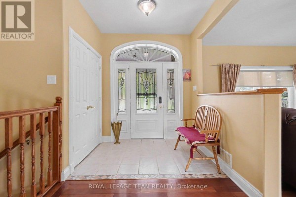 Foyer with cream walls, wood banister stairs, tiled floor, and front entrance. - 600 Crozier Road, North Grenville