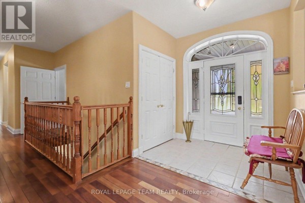 Foyer and staircase with wood flooring, banister, white double doors, and arched entryway. - 600 Crozier Road, North Grenville