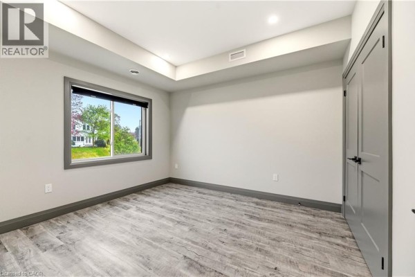 Empty bedroom with light grey walls, wood-look flooring, and a large window. - 600 Norfolk Street Unit# 104, Simcoe